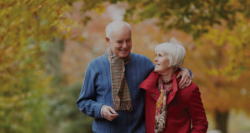 Senior couple walking in park with tree leaves all turning reds and oranges
