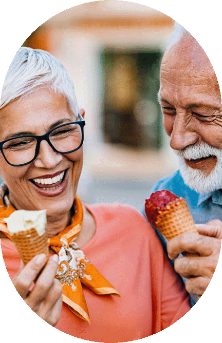 Two older adults smile and enjoy ice cream cones together outdoors during one of the lively Port Credit events. The woman wears glasses, an orange scarf, and a pink top; the man has a white beard and blue shirt. Both look happy and relaxed, soaking up the vibrant atmosphere that makes Port Credit news.